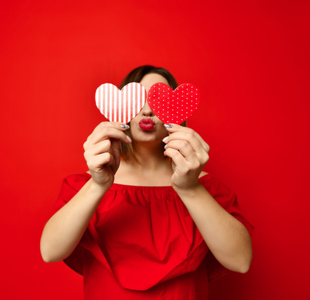 adorable girl with valentine's day heart showing love kiss fun affection portrait on red backgroundの写真素材