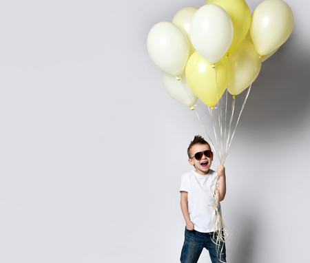 Baby boy with a bunch of balloons on a white background, wearing jeans and sunglasses. Stylish childhood partyの写真素材