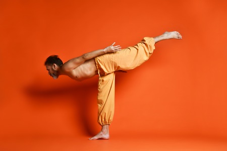 Old man practicing yoga doing stretching exercises against orange backgroundの写真素材