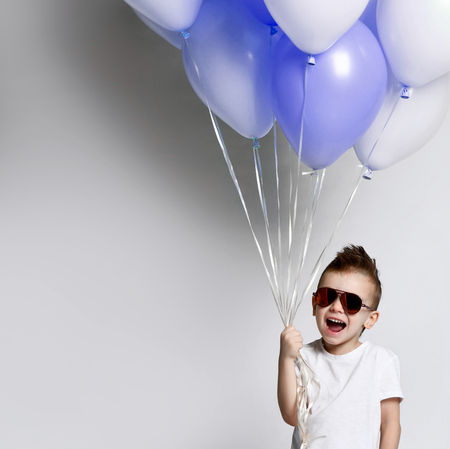 Baby boy with a bunch of balloons on a white background, wearing jeans and sunglasses. Stylish childhood partyの写真素材