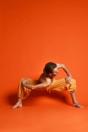 Athletic muscular senior man working out, yoga, pilates, fitness training, doing sumo squat exercises, revolved temple, goddess, sumo wrestler poseの写真素材