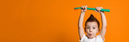 Portrait of a little boy holding a big toothbrush on his head over yellow background