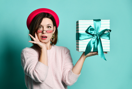Surprised beautiful woman in felt hat holding present gift box , isolated over blue backgroundの写真素材