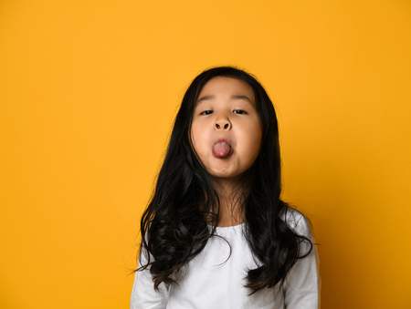 funny cute little asian girl shows the tongue over yellow wall background