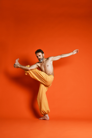 Old man practicing yoga doing stretching exercises against orange backgroundの写真素材