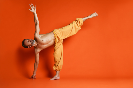 Old man practicing yoga doing stretching exercises against orange backgroundの写真素材