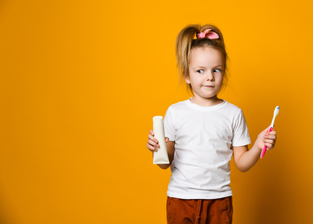 Cheerful girl with a toothbrush and toothpaste looks into the camera on a yellow backgroundの写真素材