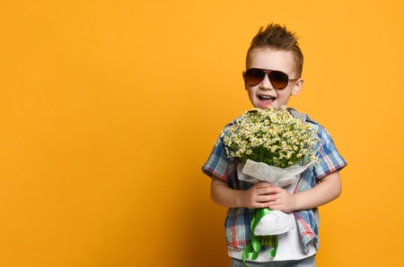 Cute little boy holding a bouquet of flowers. daisies. Mothers Day. International Women's Day. Portrait of a happy little boy on a yellow background. Spring.の写真素材