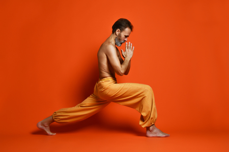 Old man practicing yoga doing stretching exercises against orange backgroundの写真素材