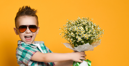 Cute little boy holding a bouquet of flowers. daisies. Mothers Day. International Women's Day. Portrait of a happy little boy on a yellow background. Spring.の写真素材