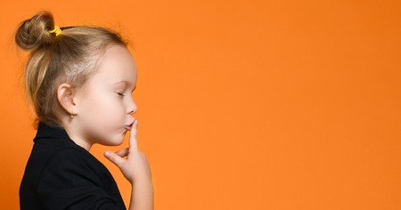 close-up close portrait on a little blonde girl, put a finger to her lips and closed her eyes and saying shh, isolated on orange backgroundの写真素材
