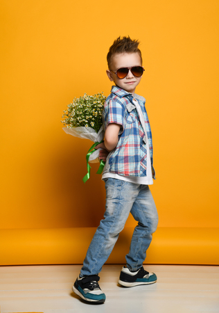 Cute little boy holding a bouquet of flowers. daisies. Mothers Day. International Womens Day. Portrait of a happy little boy on a yellow background. Spring.の写真素材