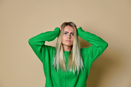 Confused handsome woman in green sweater standing touching her head and looking at camera with thoughtful face. indoor studio shoot, isolated on light backgroundの写真素材