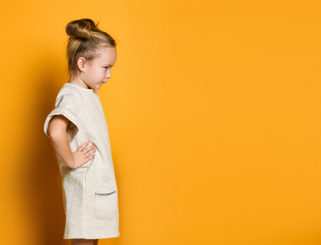 little cute girl in a light dress looks away angrily, her arms are in sides. On yellow background, sign and gesture concept, copy spaceの写真素材