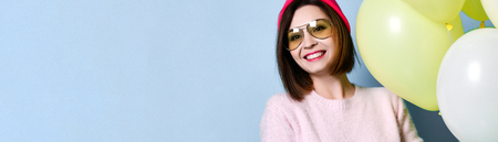 Happy pretty young woman holding air balloon in pink knitted hat on colorful blue wall backgroundの写真素材