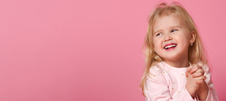 Little cute baby girl blonde in a pink suit pulls the handles in front of her and laughs looks awayの写真素材