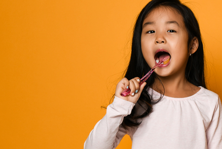 Portrait of a happy little asian girl with a big toothbrush - happily looking into the camera, ready to brush his teeth. Dentist day, teeth careの写真素材