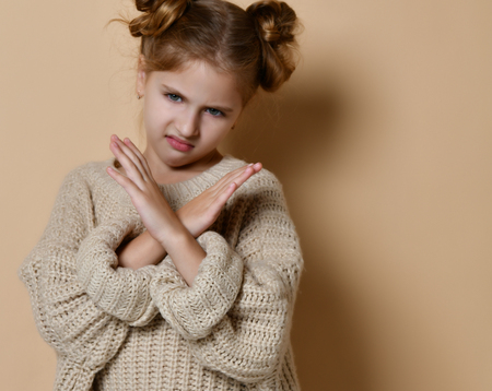 Portrait of serious, unhappy kid girl holding two arms crossed, gesturing no sign, looking away camera, isolated on beige backgroundの写真素材