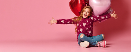 A little 7 year old girl is sitting on the floor holding a bunch of pink heart-shaped balloons. Celebrates birthday and Valentine's Day. Hangout. Birthday party.の写真素材