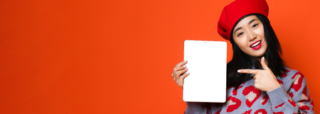 Asian girl use pad over orange background, She is showing a tablet screen , concept of technology, working, internet etc.の写真素材