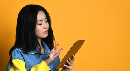 Asian girl use pad over yellow background, concept of technology, working, internet etc.
