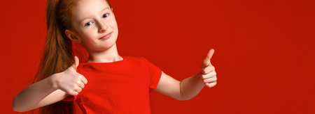 Portrait of a young teenage girl with red hair and healthy freckled skin, in a red T-shirt, looking at the camera, showing thumbs up, happy facial expressionの写真素材