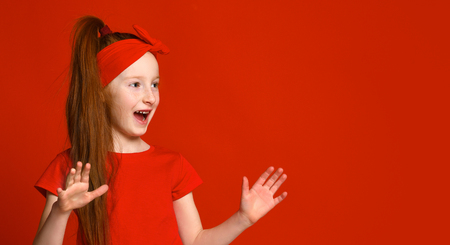 little red-haired girl with a bandage on her hair in a red t-shirt happily shouts when she sees something to the side.の写真素材