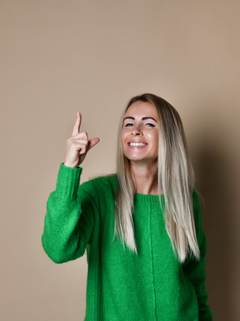 Closeup shot of nice smiling young Caucasian blonde girl isolated on beige background pointing finger up to draw attention to important information or new idea or offer.の写真素材