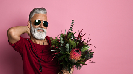 Stylish bearded middle-aged man with a modern hairstyle and fashionably dressed holding a bouquet of...