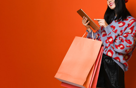 Beautiful young happy Asian woman in a stylish beret and sweater, with a colorful shopping bag using tablet for shopping online. shopping concept.の写真素材