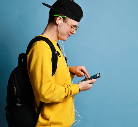 Portrait of a joyful young student in a yellow sweater listening to music with headphones and...