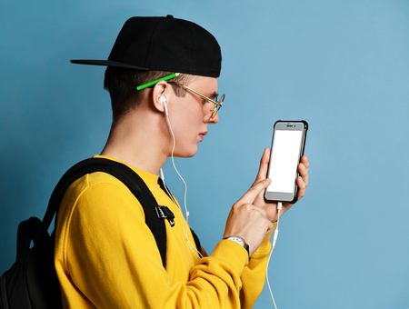 Portrait of a young student in a yellow sweater listening to music on headphones and holding a...