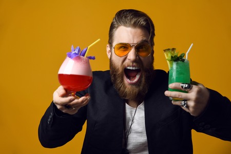 joyfully screaming bearded man with stylish hair beard holding two glasses of cocktails isolated on...