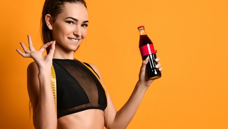 Moscow, Russia, January 2019 -  nice young fitness girl in black sportswear is looking at the camera and keeps at hand a tape measure and a bottle of sports nutrition liquid.の写真素材