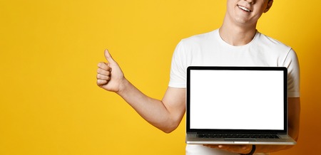 young man of the 20s in a white T-shirt holding and using a laptop, a blank white screen at the...