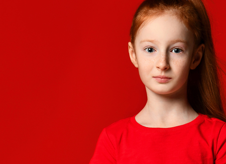 Portrait of a young gentle redhead teenage girl with healthy freckled skin, wearing a red tank top, looking at the camera with a serious or pensive expression.の写真素材