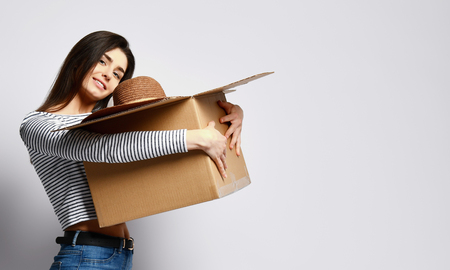 Young attractive brunette girl holding a cardboard box with things - ball, hat and others. She is dressed in jeans and a casual jersey. Raising and termination of employmentの写真素材