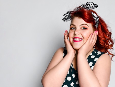 Cute portrait of a red-haired fat woman plus size in a retro polka-dot dress, joyful smiling at the camera. Pin up girl vintage.の写真素材