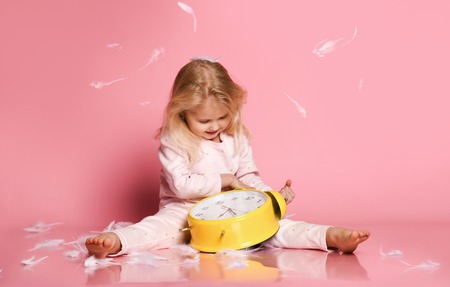 Lovely blonde babe plays with a yellow alarm clock on a pink background. just woke up in the...