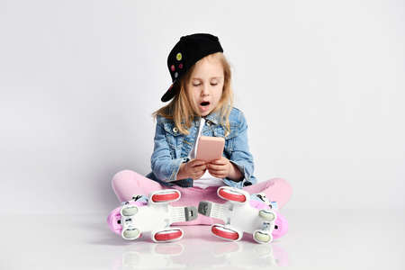 girl sitting in roller skates, wearing a blue denim and cap and smiling. The deovchka uses a mobile...