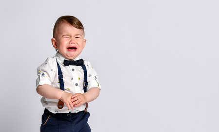 Crying baby. Portrait of a kid in full growth in the studio on a white background. Dressed in a suit...