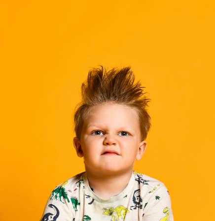 crabbed boy in a yellow T-shirt with dinosaurs on a yellow background, contorted displeased facesの写真素材