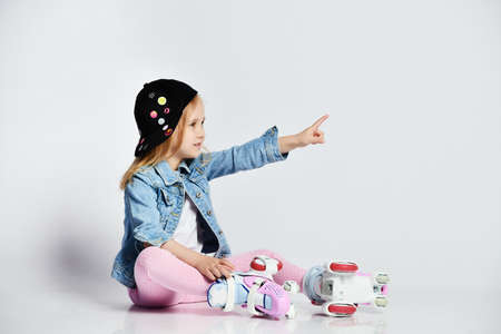 girl sits on the rollers in a blue denim and cap and smiles. The child points to the side of the...