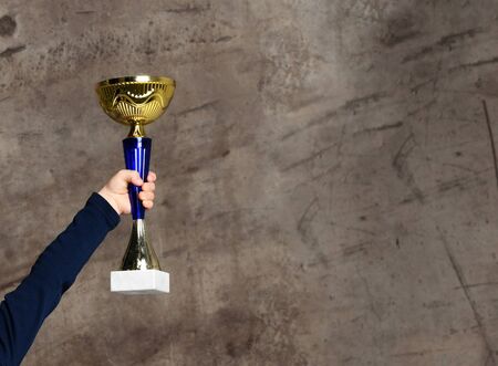 Close-up boy kid hand holding golden Trophy on concrete backgroundの写真素材