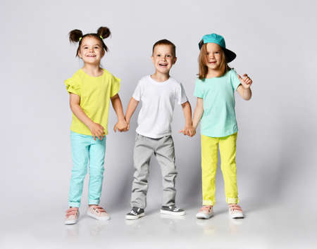Three excited kids in fashion outfits, jumping over the light background. Two sisters and brother, friends in fashionable clothes.の写真素材