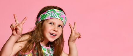 Portrait of happy cheerful girl in summer dressing for hair, showing peace gesture with two hands, isolated on pink background.の写真素材