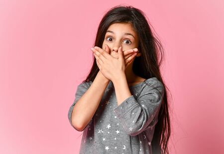 beautiful amazing frightened shocked little girl, in grey dress, posing isolated on a pink background, covering her mouth with a wallの写真素材