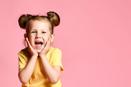 Portrait of a little blonde girl holding hands on her head, screaming with an open mouth and a crazy...