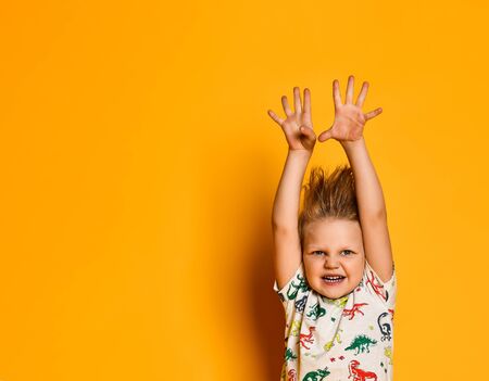 Little cute blond boy preschooler in pajamas with dinosaurs having fun has joy in the studio over...