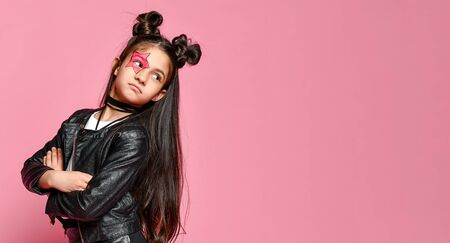 hipster punk girl - dressed in a leather jacket and skirt, with a funny hairstyle and a makeup painted star on her face, folded her arms across her chest and looks behind her.の写真素材